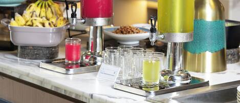 Een bar met een drankdispenser, een fruitschaal en een buffetopstelling.