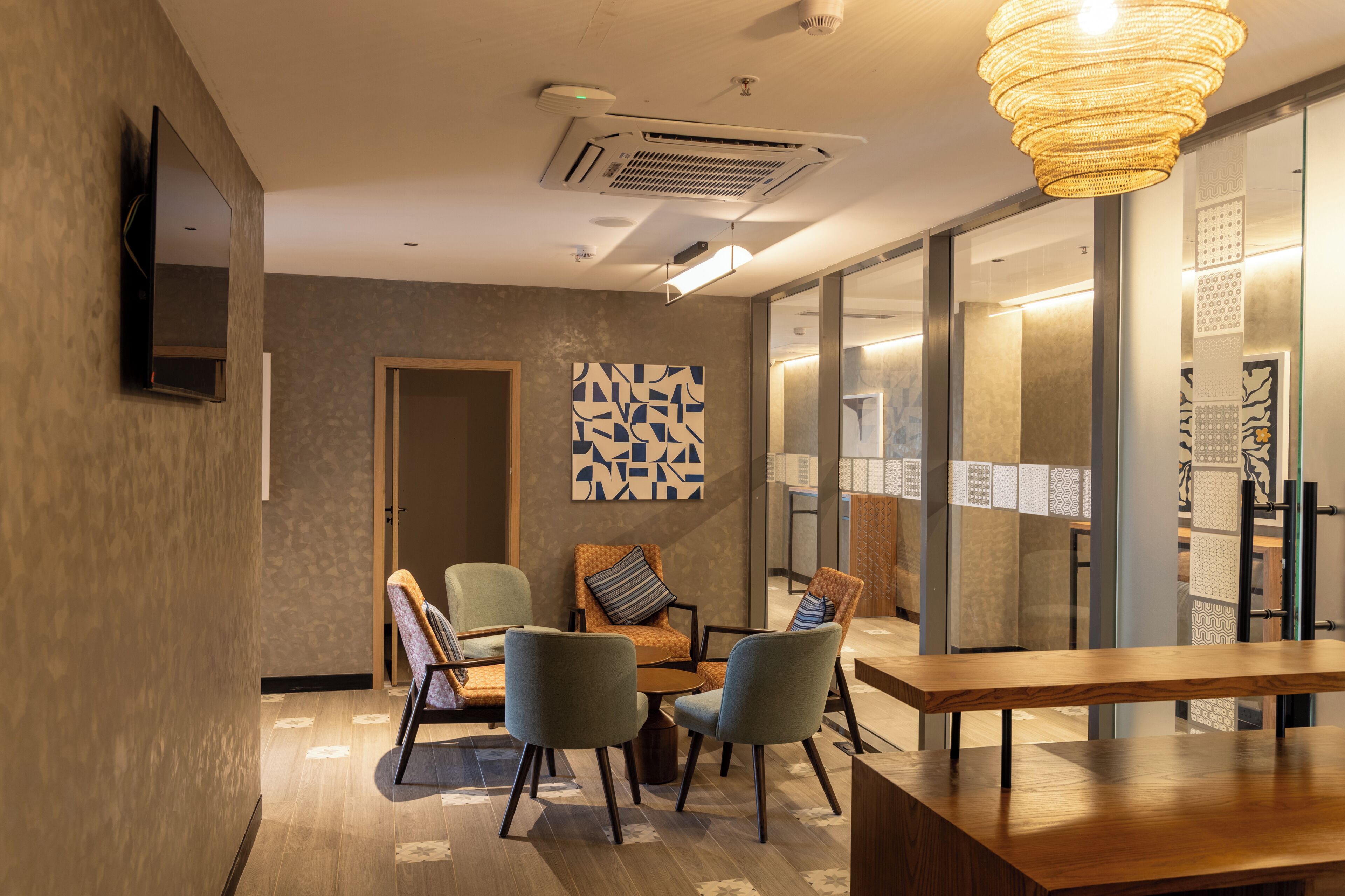 A modern meeting room with a wooden table, four chairs, a wall-mounted TV, and a decorative light fixture.
