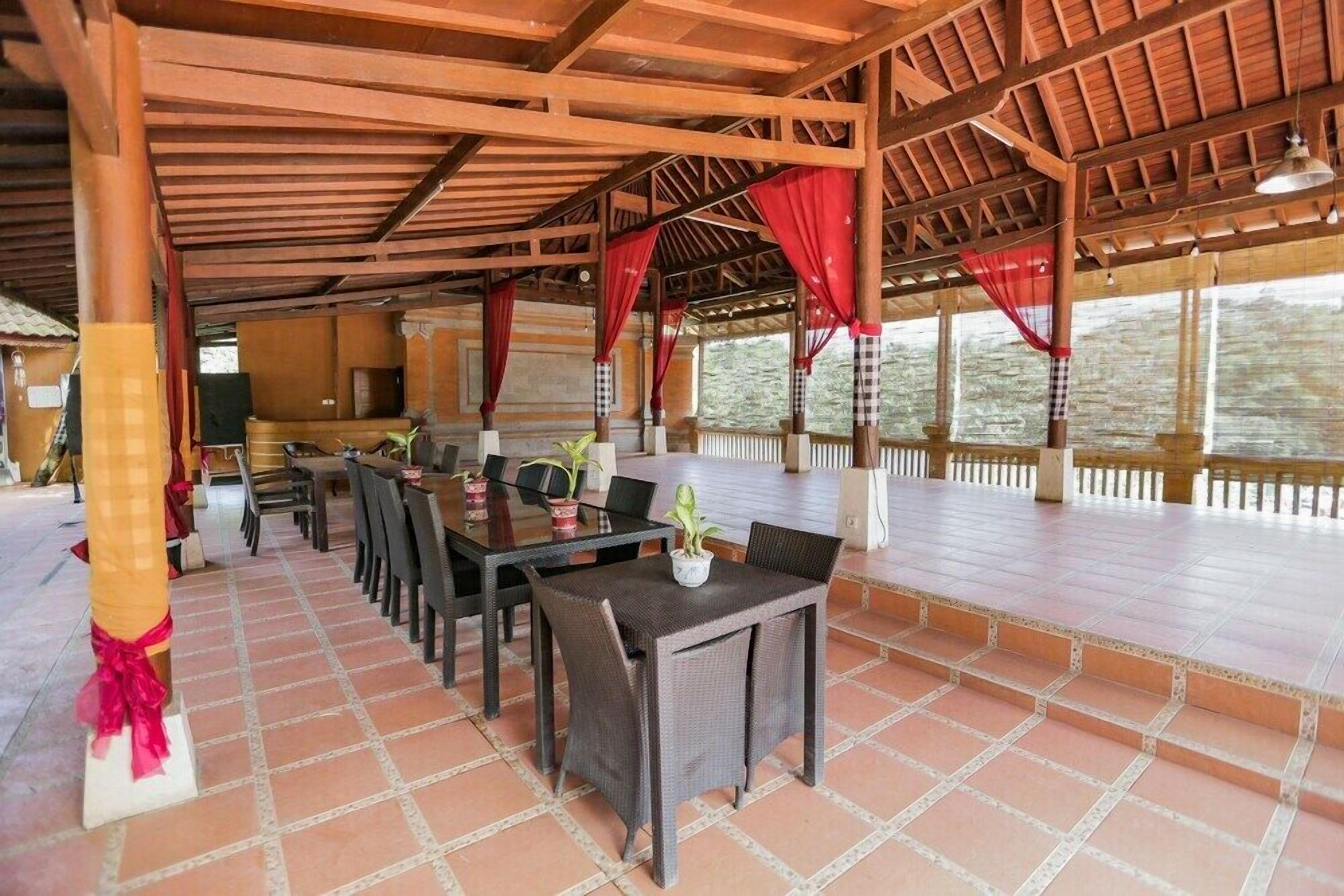 A covered outdoor dining area with tables and chairs, a tiled floor, and a wooden ceiling structure.