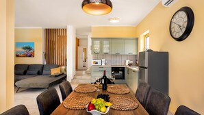 A modern kitchen with a dining area, featuring a wooden table with a fruit bowl, a wine bottle, and a clock on the wall. - Villa Isla Blue 2 pool&welness Krk by Villas Guide (Vrbnik)