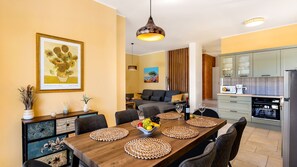 Ein modernes Wohnzimmer mit einer Couch, einem Esstisch mit Platzsets und einer Küchenzeile mit Geräten.