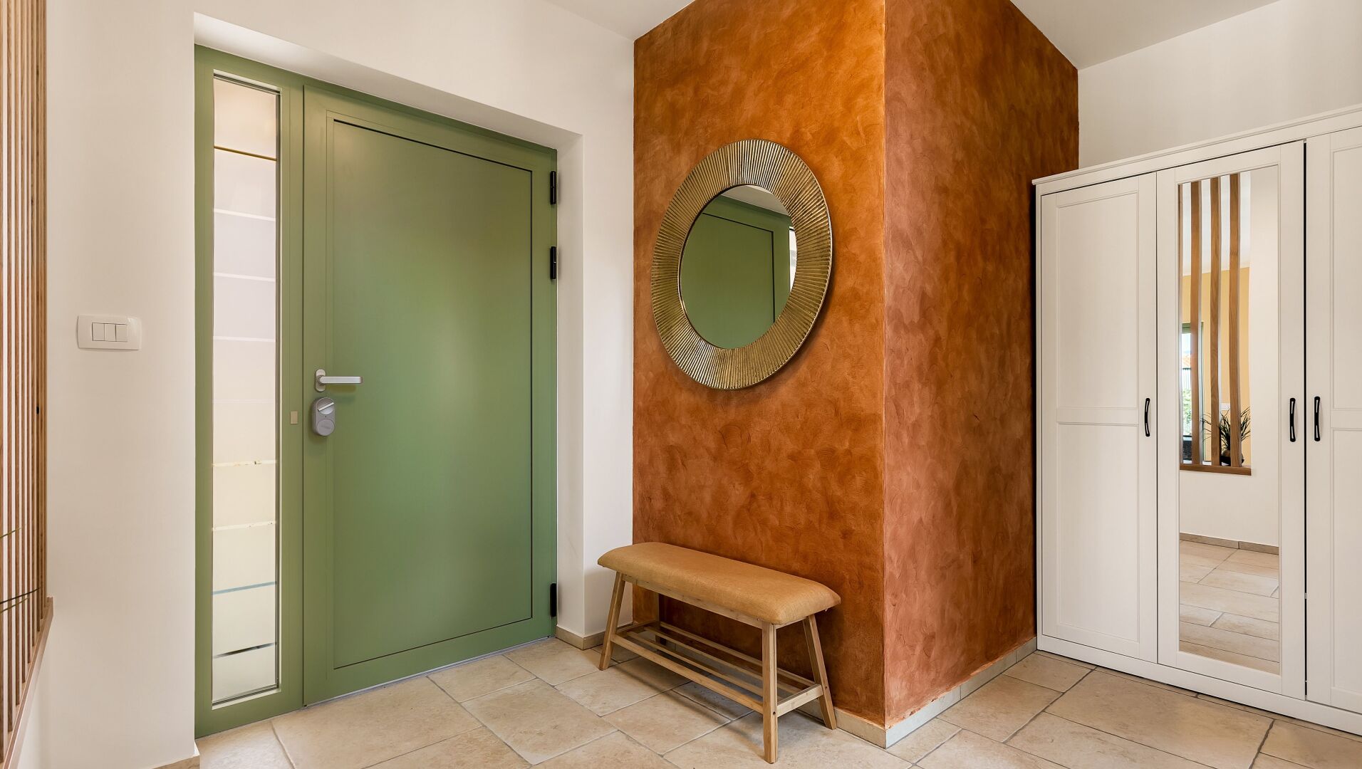 A hallway with a green door, a bench, a mirror, and a white cabinet.