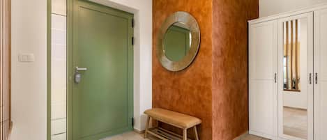 A hallway with a green door, a bench, a mirror, and a white cabinet.