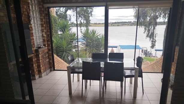 Comedor con mesa y sillas de vidrio, pared de ladrillo y vista a un lago.