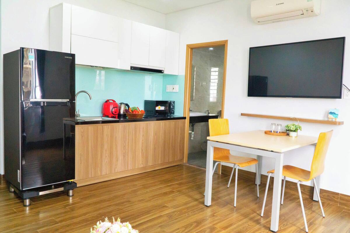 Een moderne keuken met een zwarte koelkast, houten kastjes, een magnetron en een eethoek met een tafel en stoelen.