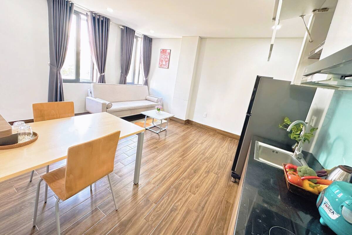Een moderne woonkamer met een bank, een eettafel en stoelen. Er is een keuken met een koelkast en een spoelbak.