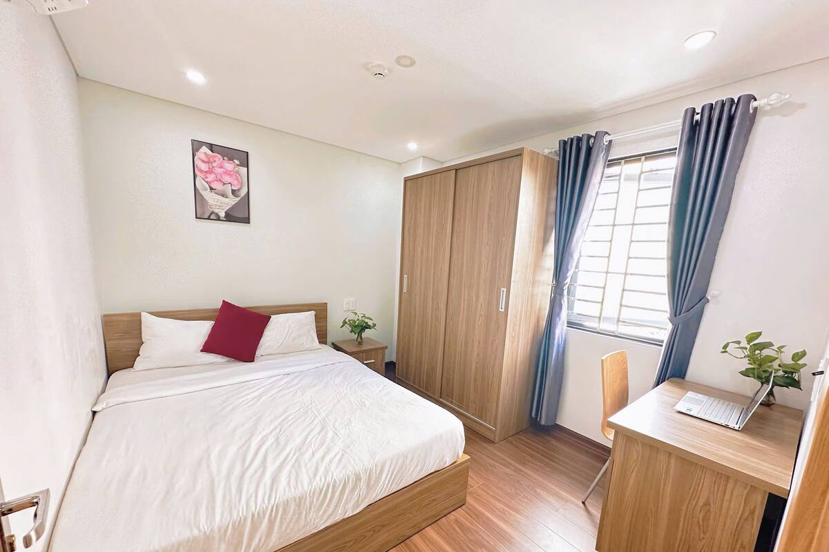 Een slaapkamer met een bed, een bureau, een kledingkast en een raam met gordijnen.