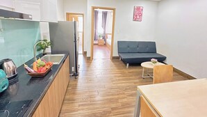 A modern kitchen with a refrigerator, stove, and sink. There is a dining area with a sofa and a small table. A hallway leads to a bedroom. - Gold Hotel & Apartment Da Nang (Da Nang)