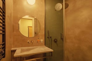 Ein Badezimmer mit rundem Spiegel, Waschbecken, Dusche und Handtuchhalter.