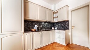 Une cuisine avec des meubles blancs, un plan de travail en marbre et un parquet en bois disposé en chevrons.