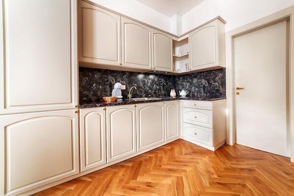 A kitchen with white cabinetry, a marble countertop, and a herringbone wood floor. - Hotel La Bohemia (Karlovy Vary)