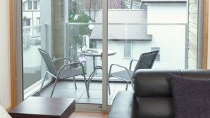 A modern living room with a leather sofa, a small table, and two chairs. A sliding glass door leads to an outdoor balcony with a table and chairs. - Bluebird Chalets (Hakuba)