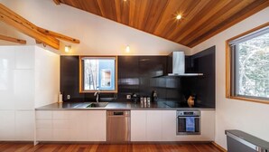 A modern kitchen with wooden ceiling beams, a built-in dishwasher, and a window providing natural light. - Bluebird Chalets (Hakuba)