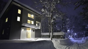 A two-story building with a balcony and a snow-covered landscape at night. - Bluebird Chalets (Hakuba)
