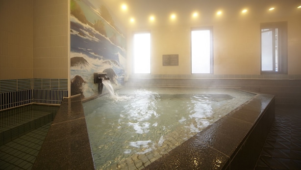 Un bain à remous agrémenté d’une cascade, avec des murs carrelés et une vue sur l’extérieur grâce à de grandes fenêtres.