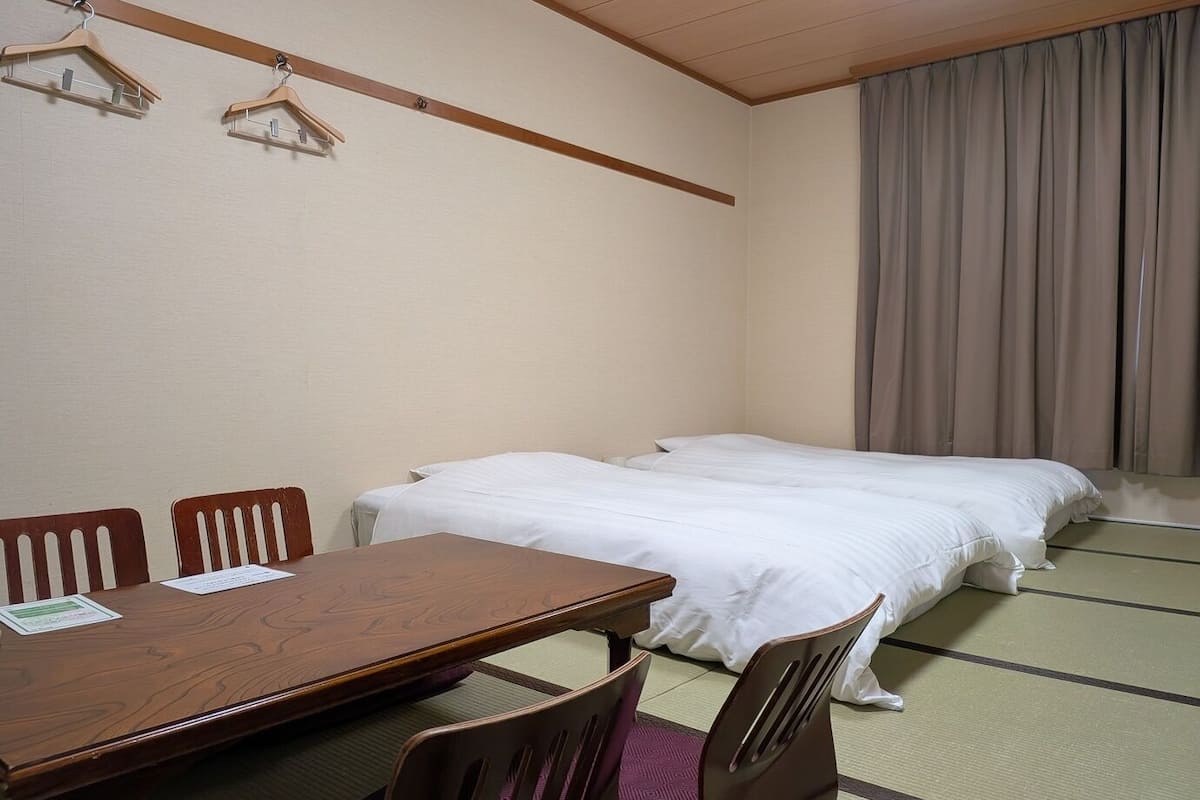 A hotel room with a wooden table, two beds, and a futon.