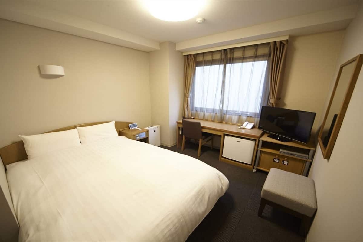 A hotel room with a bed, desk, television, and a small seating area.