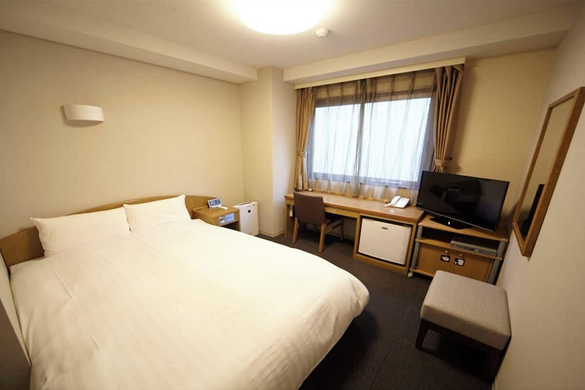 A hotel room with a bed, desk, chair, TV, and a small refrigerator.