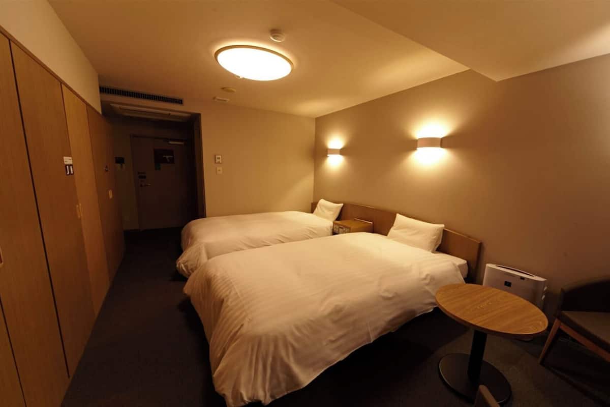A hotel room with two beds, a small round table, a chair, and a wardrobe.