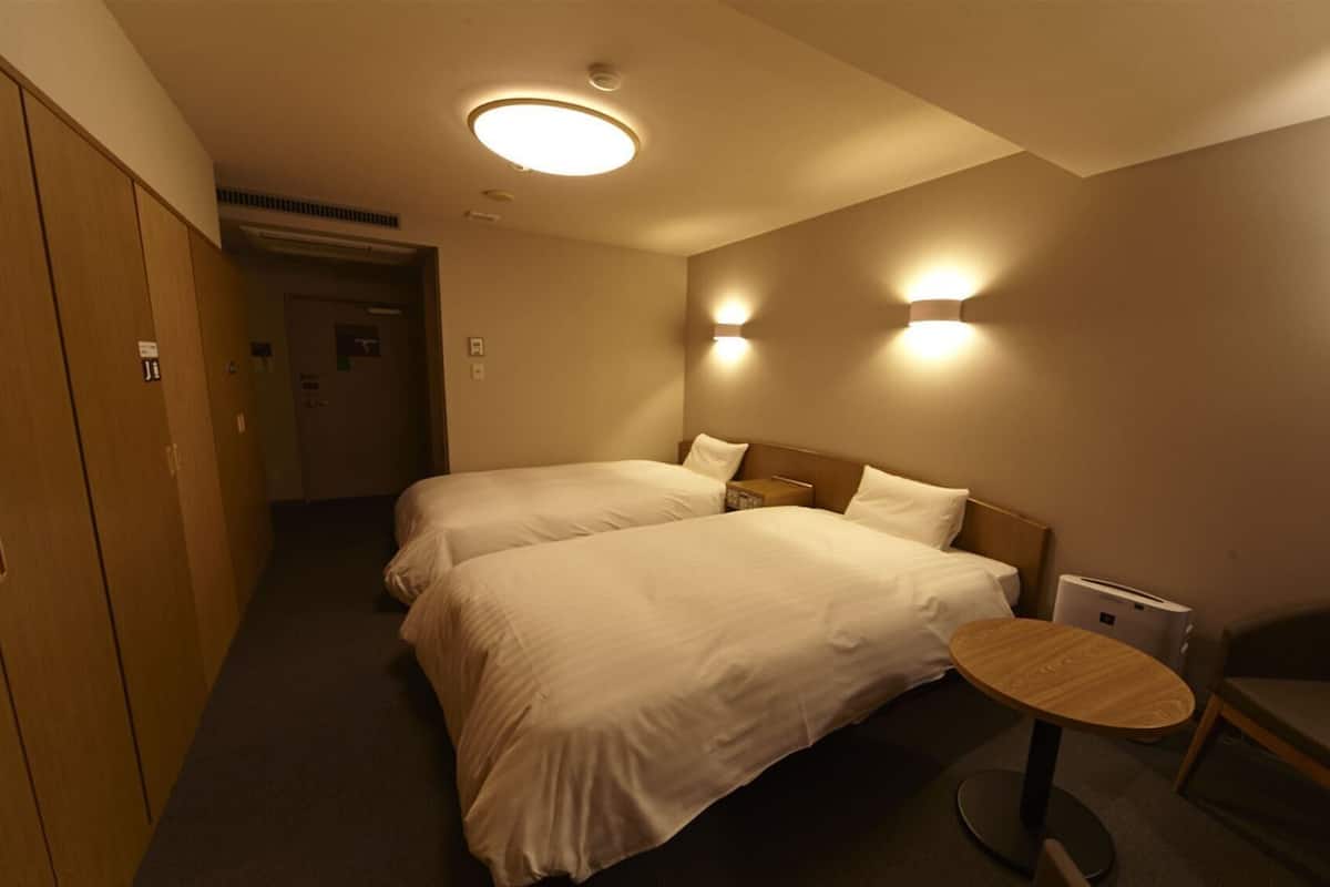 A hotel room with two beds, a small round table, a chair, and a wardrobe.