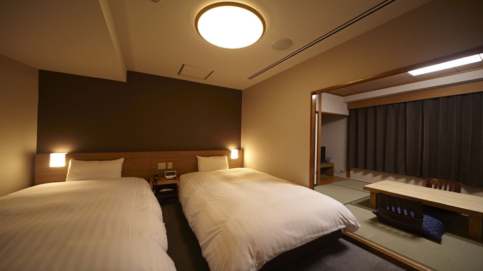 A hotel room with two beds, bedside tables, a mirror, and a small desk with a chair.