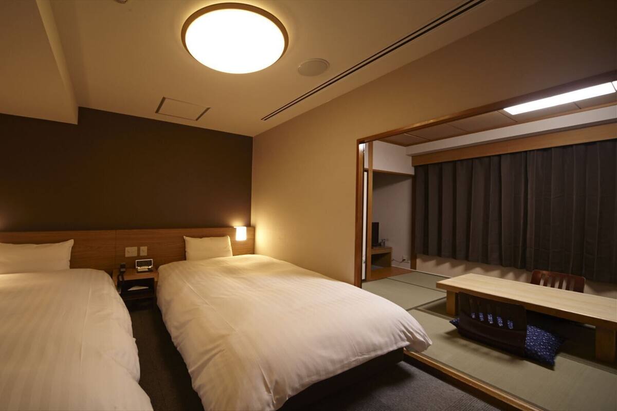A hotel room with two beds, bedside tables, a mirror, and a small desk with a chair.