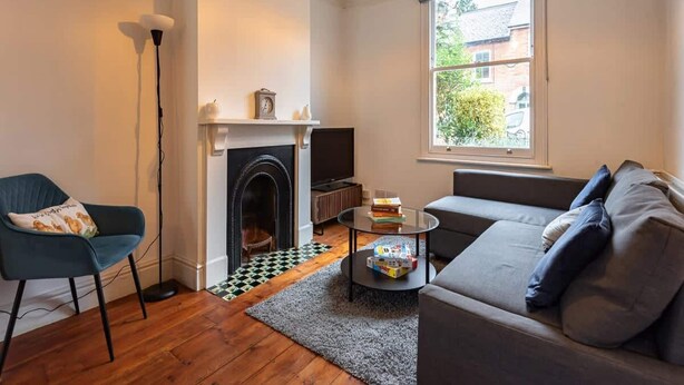 A living room with a fireplace, a sofa, a coffee table, and a large window. - Cosy Holiday Home in Berkshire (Reading)