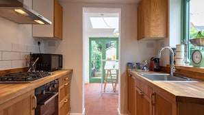 A modern kitchen with wooden cabinets, a stainless steel range hood, and a window overlooking a garden. - Cosy Holiday Home in Berkshire (Reading)