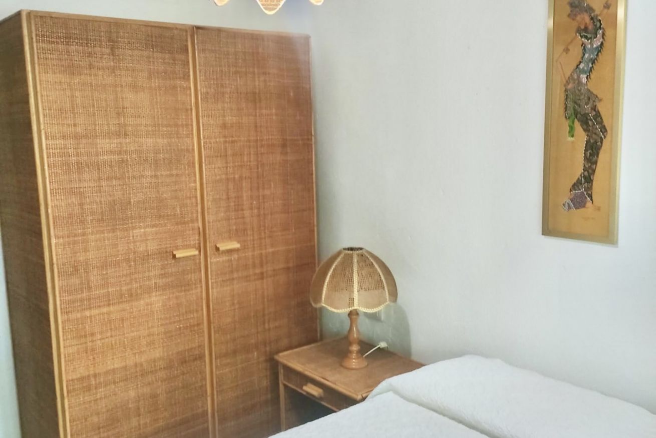 A room with a large wardrobe, a bedside table with a lamp, and a painting on the wall.