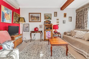 A living room with a TV, sofa, coffee table, and artwork on the walls. - Colour Pop Cottage - A vibrant courtyard retreat perfect for long stays (Payneham)