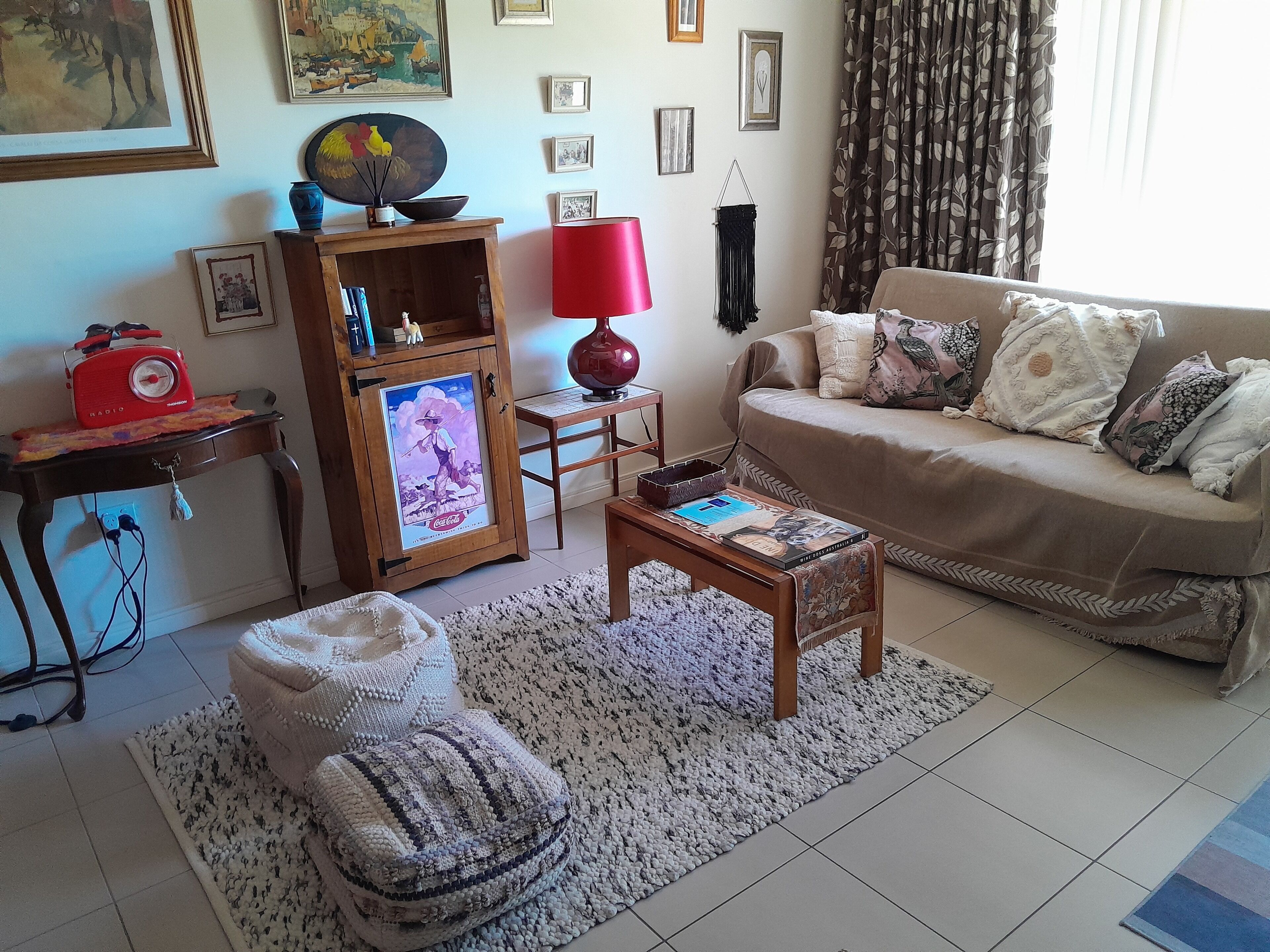 Ein gemütliches Wohnzimmer mit einer Couch, einem Couchtisch, einem Holzkasten mit einem Coca-Cola-Poster, einer roten Lampe und einem gemusterten Teppich.