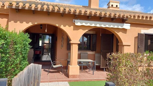 Ein Gebäude mit einem Ziegeldach, zwei Bögen und einer kleinen Terrasse mit Tisch und Stühlen.