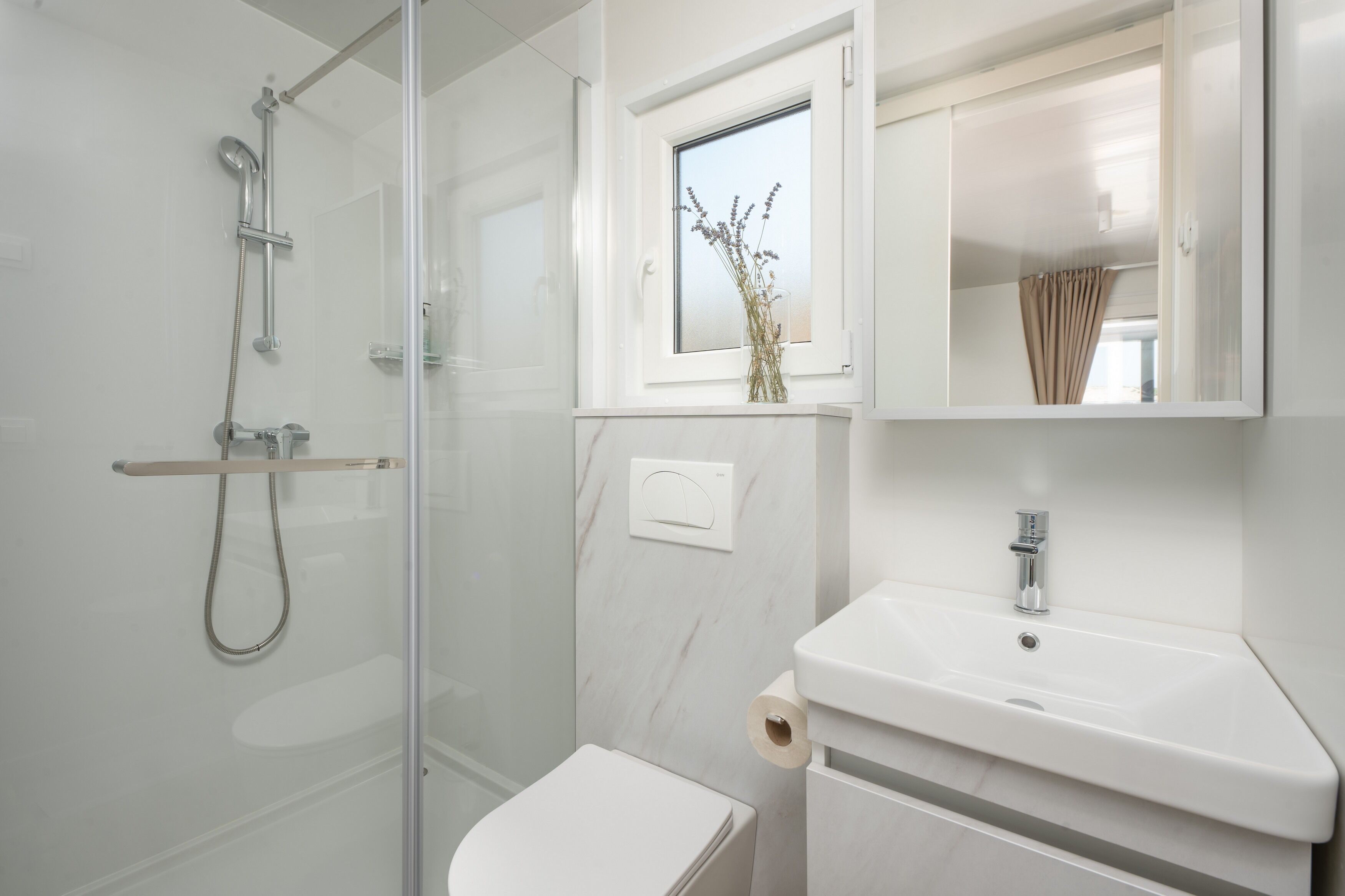 Un bany modern amb dutxa de vidre, un vàter i un lavabo amb una finestra a sobre.