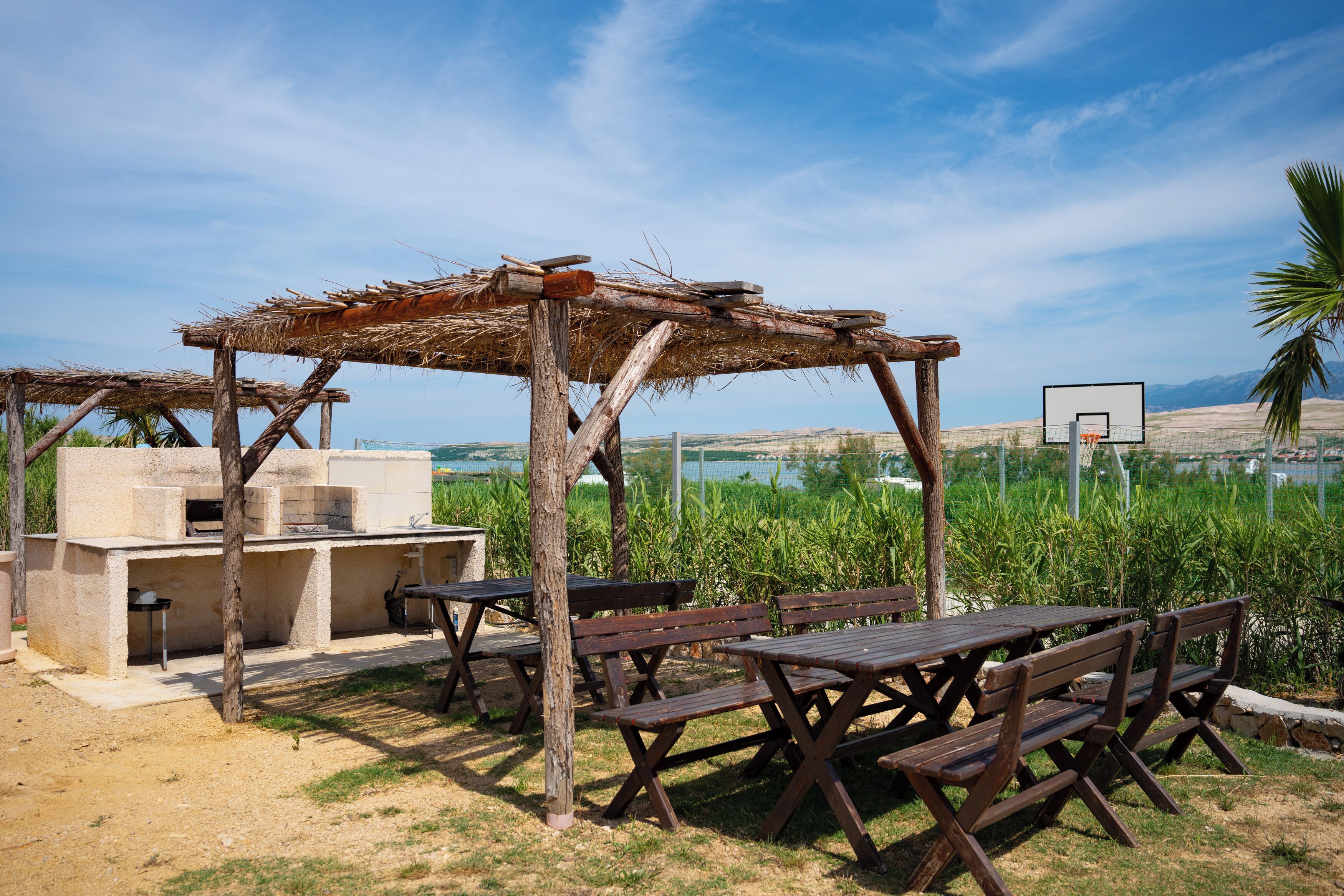 Un espace extérieur aménagé avec des bancs en bois et un barbecue, offrant une vue sur un plan d’eau et des montagnes.