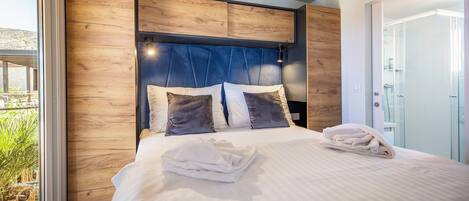 A modern bedroom with a wooden headboard, a large bed with white linens, and a glass shower enclosure.