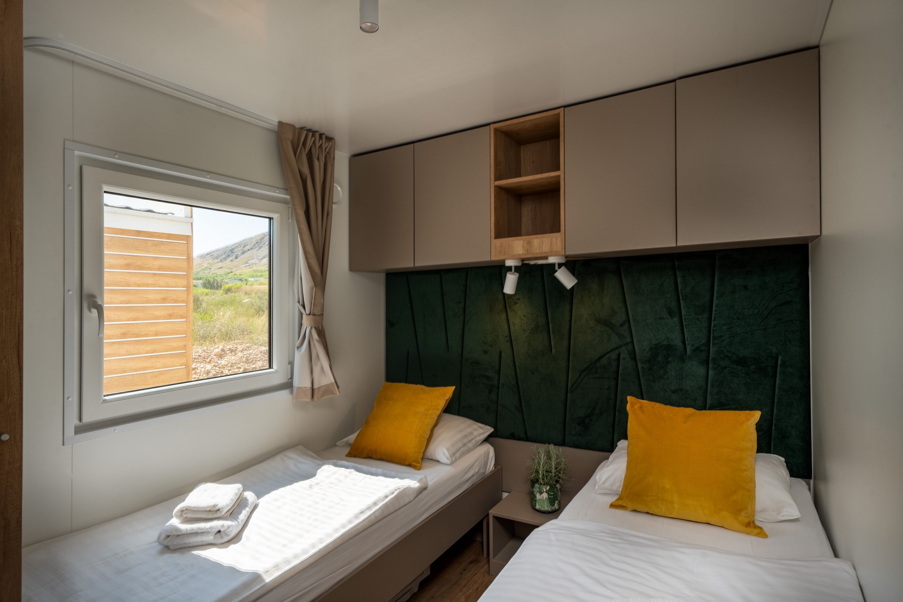 A bedroom with two beds, a window with curtains, a green headboard, and built-in shelves.