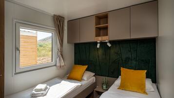 A bedroom with two beds, a window with curtains, a green headboard, and built-in shelves.