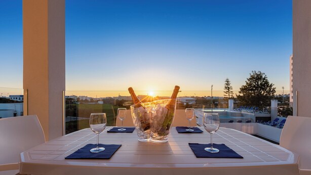 Ett bord dukat för två personer, med en stor skål full av is och champagneflaskor, med utsikt över en pool och en stadsbild i solnedgången.