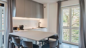 Una cocina moderna con una isla grande, gabinetes grises y vistas a árboles por la ventana.