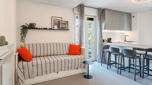 Una sala moderna con un sofá a rayas, una mesita redonda y una cocina con taburetes de bar.