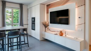 Una cocina moderna con televisor integrado, armarios blancos y un comedor con mesa y sillas.