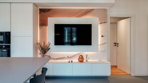 Una cocina moderna con televisor integrado, armarios blancos y un comedor con sillas.