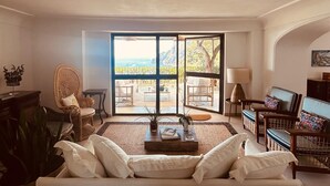 Ein geräumiges Wohnzimmer mit einer großen Couch, einem Essbereich mit Stühlen und Meerblick durch große Glaswände.