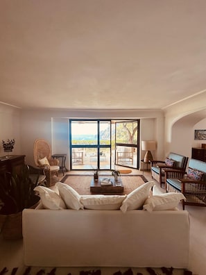 A spacious living room with a large sofa, a dining area with chairs, and a view of the ocean through large glass doors. - Villa Volare, Capri (Capri)