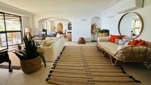 Ein geräumiger Wohnbereich mit großem Fenster, einer Couch, einem Sessel, einem runden Spiegel und einem Teppich.