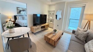 Un salon moderne comprenant un téléviseur à écran plat, un canapé, une table basse, une table à manger et une petite table d’appoint avec une lampe.