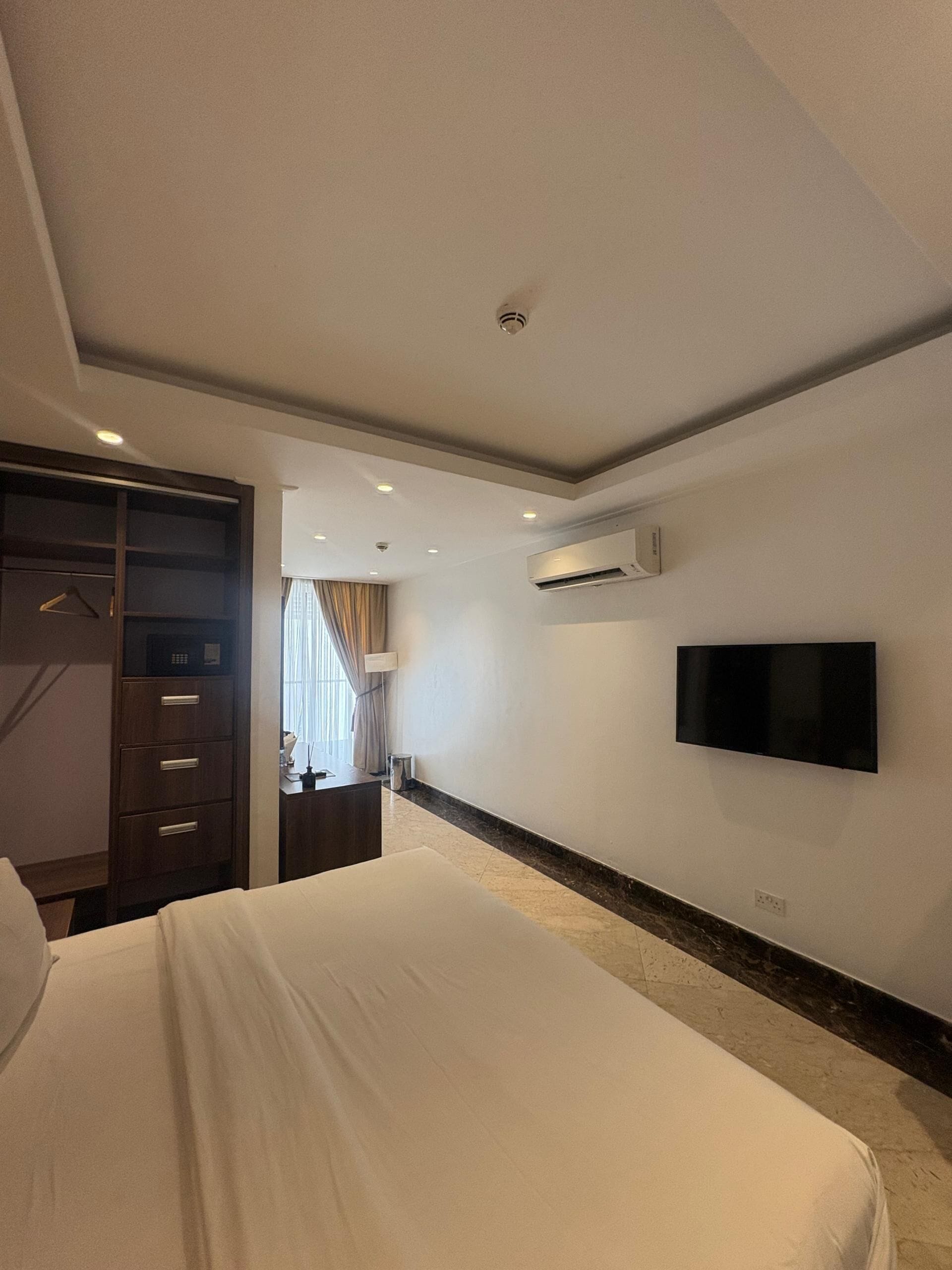 A hotel room with a bed, a wardrobe, a desk, a TV, and an air conditioning unit.