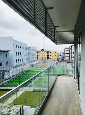 Un balcon donnant sur un terrain de sport, des immeubles et une grue rouge.