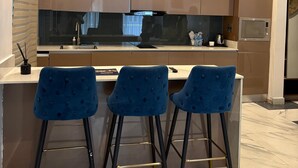 Cozinha moderna com ilha central, três banquetas azuis e iluminação pendente.