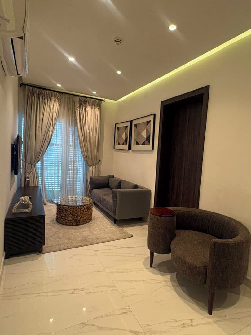 A modern living room with a sofa, a round coffee table, a TV, and a large window with curtains.
